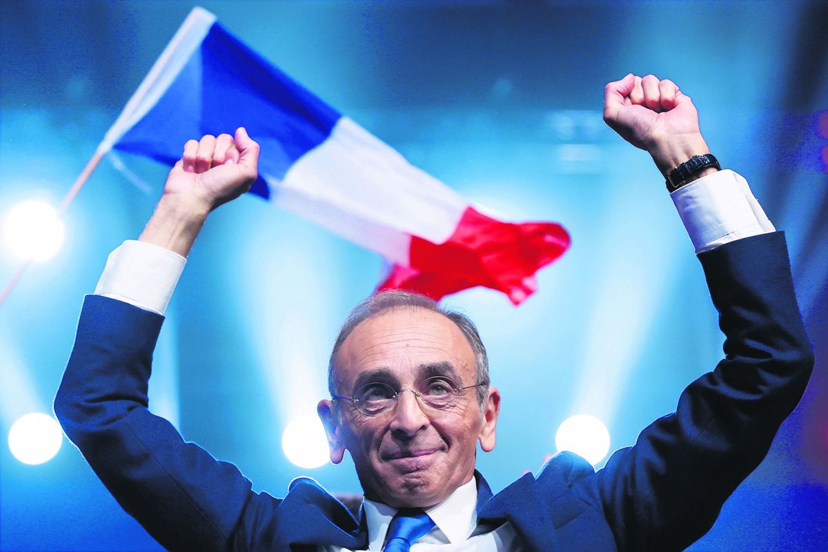 Eric Zemmour mitingde elleri havada şekilde gülümsüyor.