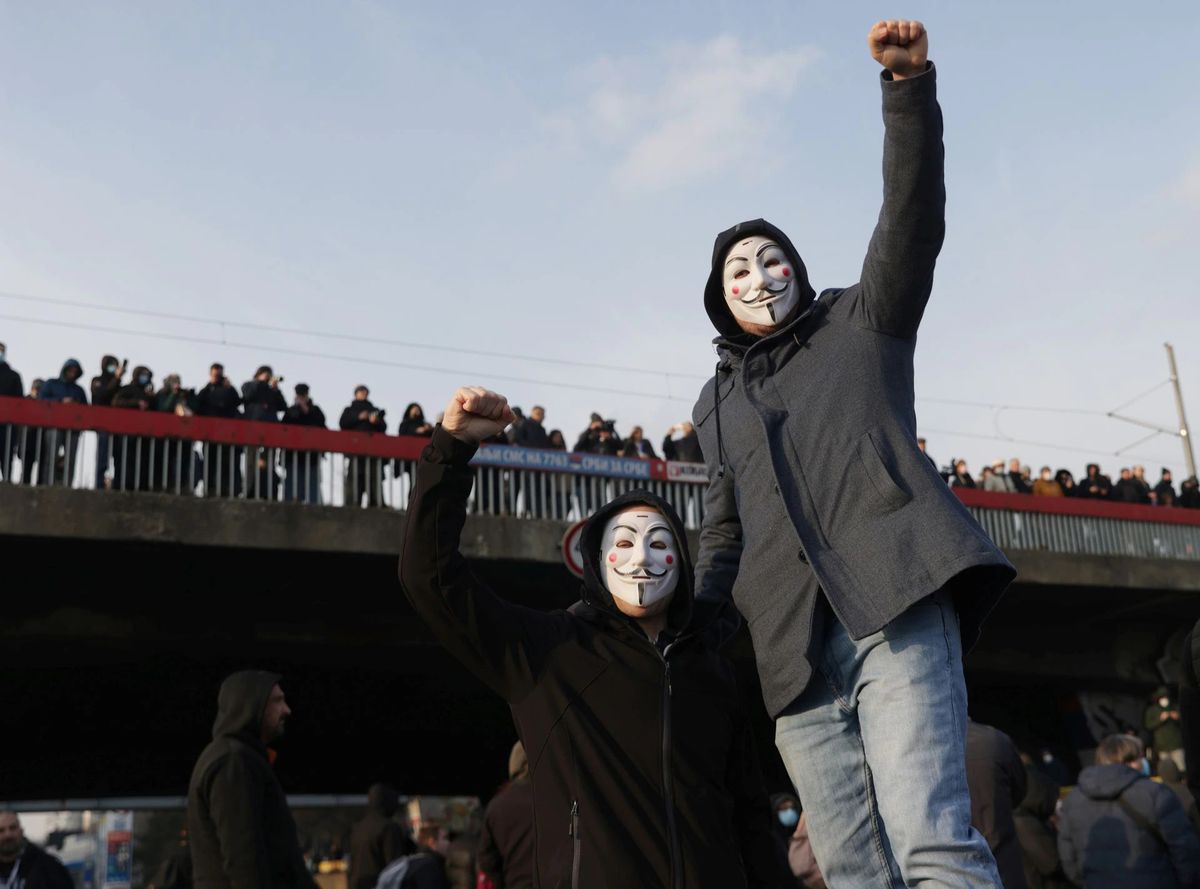 Sırbistan'da V for Vandetta maskeli iki kişi protestoda poz vermiş. Biri ayakta diğeri oturuyor ve ellerini yumruk yapmışlar.