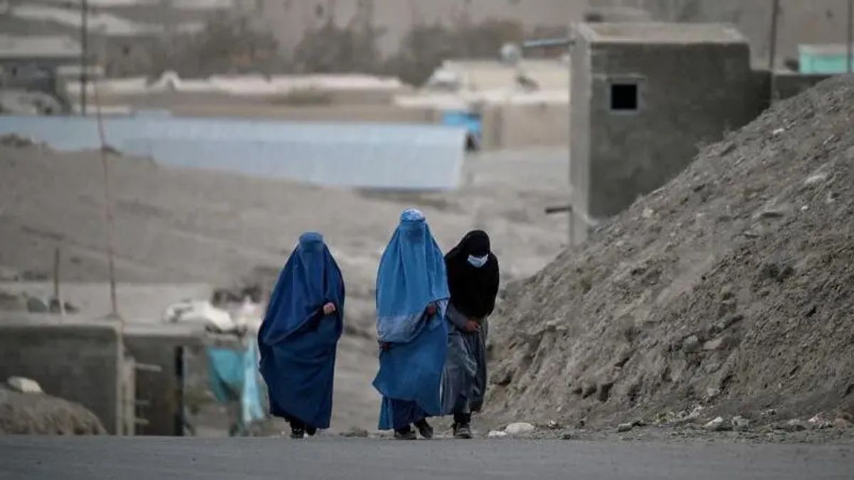 Afganistan'da 3 kadın yolda yürüyor. Kadınlardan 2'si burka giymiş, diğeri iste yüzünü tamamen kapatmış